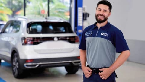 Mecânico do Centro Automotivo, sorri de forma amigável em frente a um carro, transmitindo confiança no serviço.